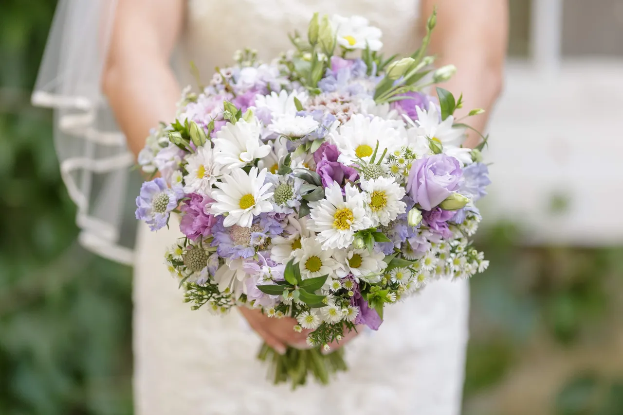 A bride holding a hand-tied bridal bouquet of white, purple, and yellow flowers.