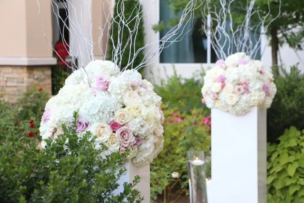 Elegant floral arrangements on white pedestals with hydrangeas and roses, accented with white branches.