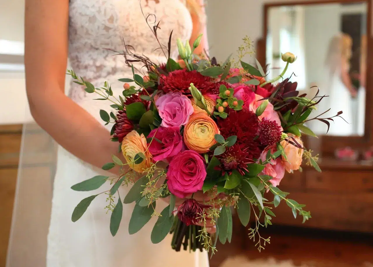 Bride holding a vibrant wedding bouquet with roses, ranunculus, and eucalyptus.