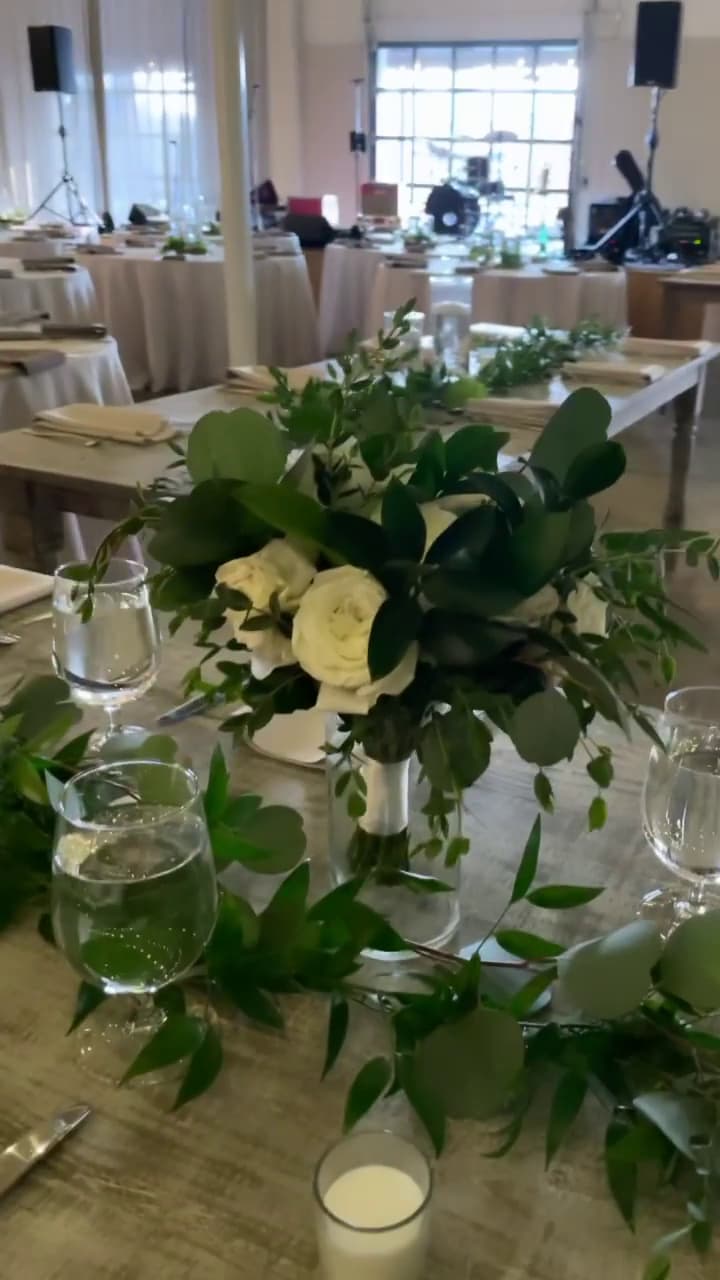 Rustic wedding reception table featuring white roses in a centerpiece and lush greenery table runner at The Stave Room, Atlanta.