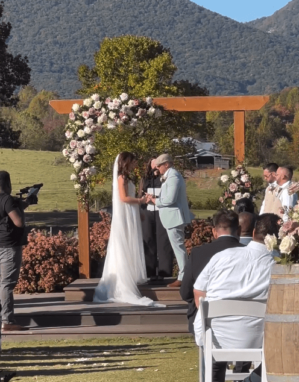 A bride and groom exchanging vows under a rustic wooden arch decorated with lush floral arrangements by our wedding floral services