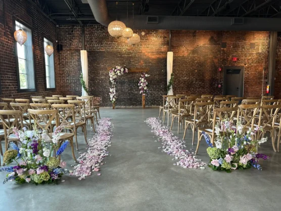 Aisle decorated with purple wedding flowers and rose petals leading to a floral arch at an elegant indoor ceremony venue.