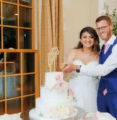 Bride and groom cutting a tiered wedding cake decorated with soft pink and white wedding cake flowers.