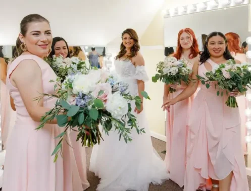 Bride and bridesmaids holding lush bridal bouquet and bridesmaids bouquets with white, blush, and greenery accents.