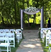 Outdoor wedding aisle with white chairs and elegant ceremony flowers decorating the path and arch.