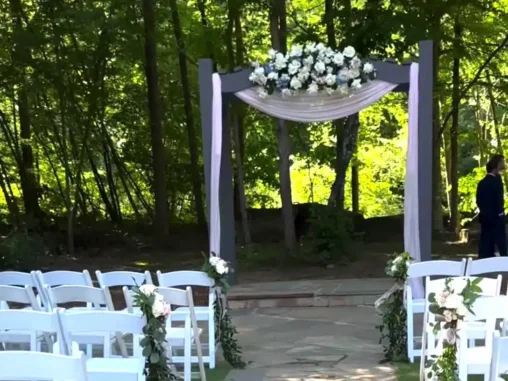 Outdoor wedding aisle with white chairs and elegant ceremony flowers decorating the path and arch.