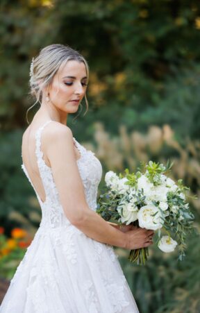 Bride holding a lush bride bouquet of white and green flowers, looking serenely to the side with a green background.