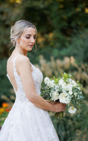 Bride holding a lush bride bouquet of white and green flowers, looking serenely to the side with a green background.