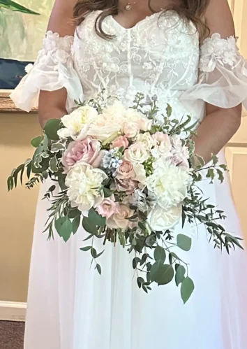 Bride holding a summer bridal bouquet featuring white, blush, and soft pink flowers with lush greenery.