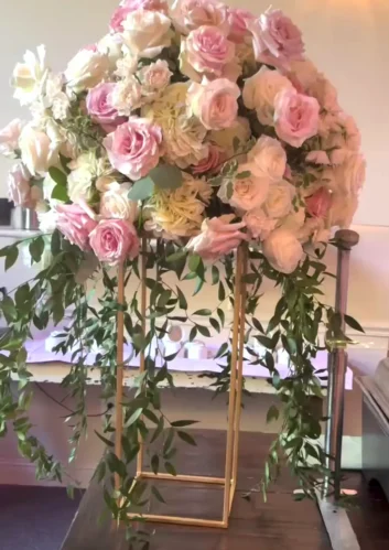 A stunning summer wedding centerpiece featuring pink and white roses with cascading greenery in a gold stand.