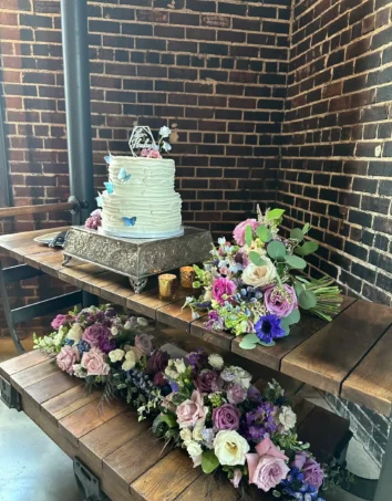 Wedding cake surrounded by vibrant Fall wedding flowers, including roses and seasonal blooms, on a rustic wooden table.