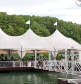 A tented wedding reception setup on a pier extending over the water at Lake Lanier, surrounded by lush greenery.