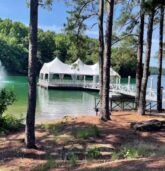 A scenic view of a tented wedding reception venue on a pier extending over a lake, surrounded by trees at Lake Lanier.