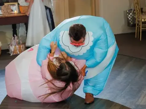 Couple playfully wrestling in inflatable costumes during a summer wedding gender reveal celebration.