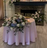 Sweetheart table with lush floral arrangement in front of a fireplace floral decoration featuring white, blush, and blue flowers.