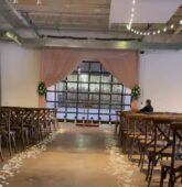 Romantic wedding ceremony aisle at The Stave Room in Atlanta, featuring white rose petals lining the walkway and a soft pink draped backdrop with greenery accents