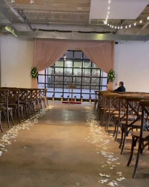 Romantic wedding ceremony aisle at The Stave Room in Atlanta, featuring white rose petals lining the walkway and a soft pink draped backdrop with greenery accents