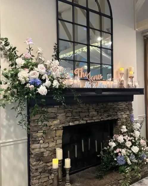 Elegant fireplace floral decoration with white and blush flowers, candles, and greenery.