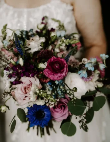 Bride holding a vibrant purple bridal bouquet with mixed flowers, including roses and ranunculus.