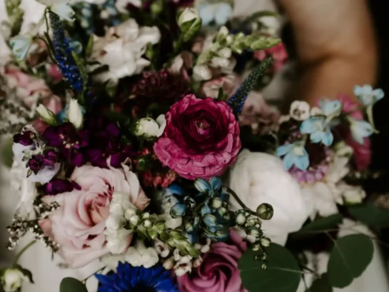 Bride holding a vibrant purple bridal bouquet with mixed flowers, including roses and ranunculus.