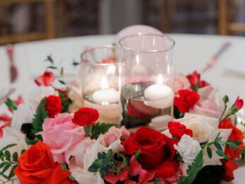 Elegant table floral arrangement with red, pink, and white roses surrounding candles.