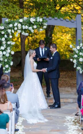 Bride walking down the aisle under an arch adorned with wedding ceremony flowers.