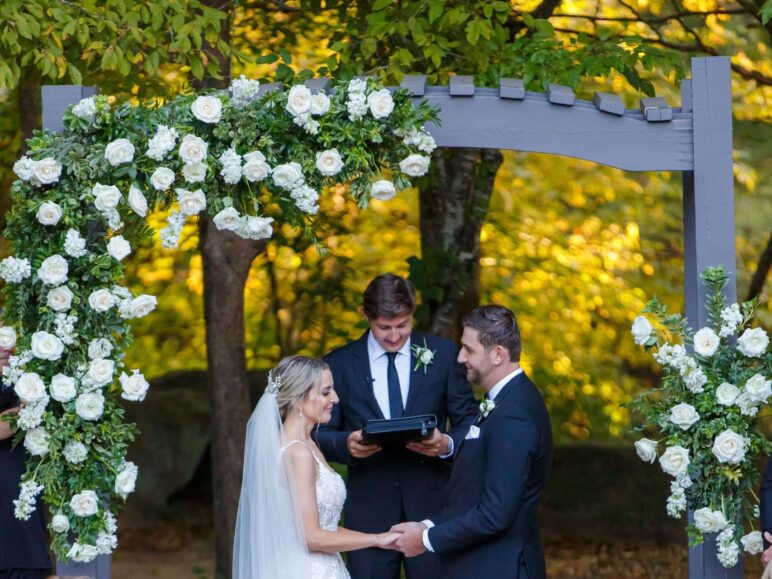 Bride walking down the aisle under an arch adorned with wedding ceremony flowers.