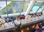 Overhead view of a wedding reception at a high-rise venue with guests seated around a long table adorned with large, colorful floral centerpieces.