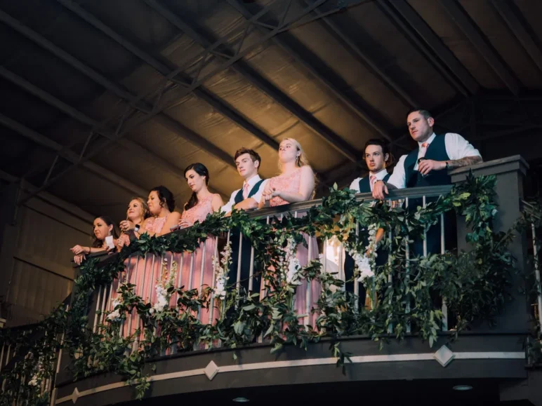 Wedding party on a balcony decorated with greenery and flowers.