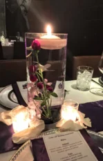 Candle centerpiece with flowers submerged in water at an elegantly set dinner table.
