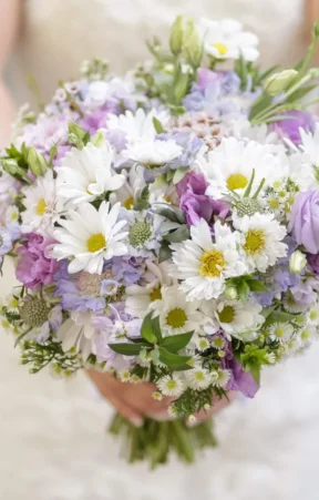 A bride holding a hand-tied bridal bouquet of white, purple, and yellow flowers.