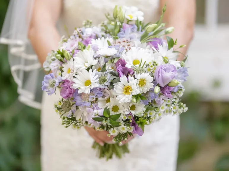 A bride holding a hand-tied bridal bouquet of white, purple, and yellow flowers.