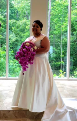Bride in a white gown holding a large cascading bridal bouquet of purple orchids and mixed flowers.