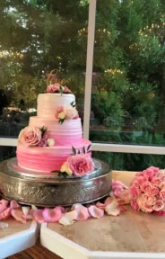 Wedding cake decorated with pink flowers and surrounded by guest wedding table arrangement