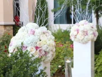 Elegant floral arrangements on white pedestals with hydrangeas and roses, accented with white branches.