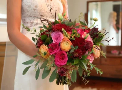 Bride holding a vibrant wedding bouquet with roses, ranunculus, and eucalyptus.