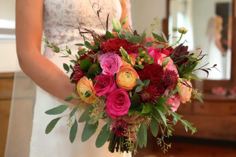 Bride holding a vibrant wedding bouquet with roses, ranunculus, and eucalyptus.