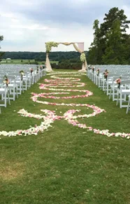 Outdoor wedding ceremony setup with a floral arch and petal aisle decorations.