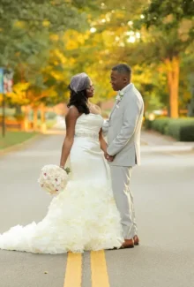 A bride and groom holding hands in the middle of a tree-lined street, with the bride holding a bouquet from our wedding floral services