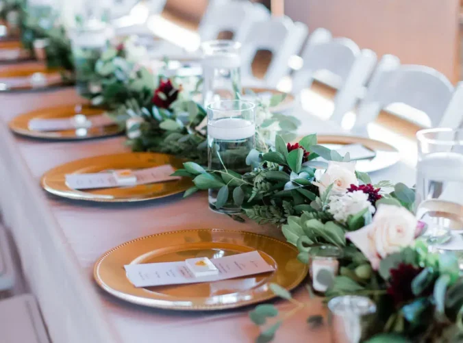 A long wedding table with elegant place settings and a floral and greenery runner decorated with candles