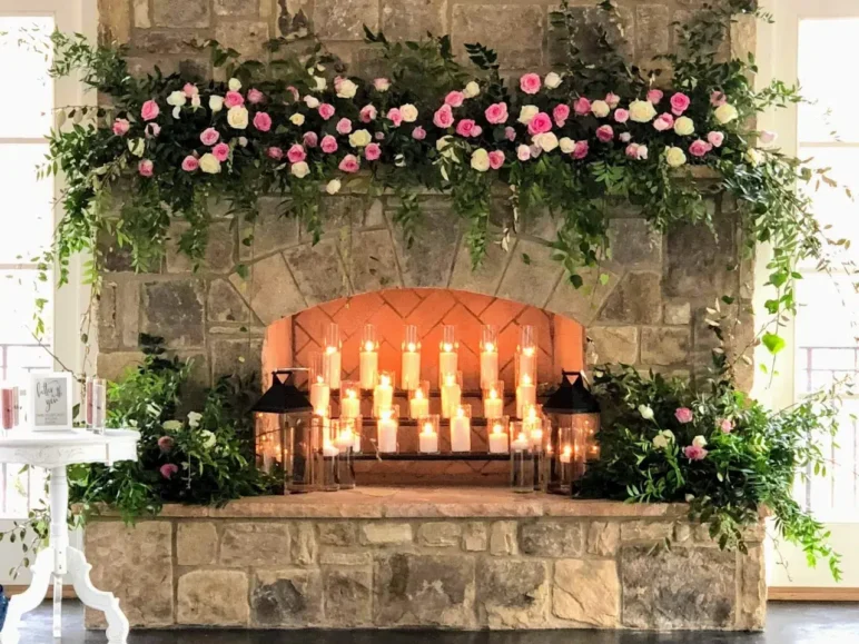 Elegant wedding fireplace decorated with greenery, pink and white roses, and numerous candles.