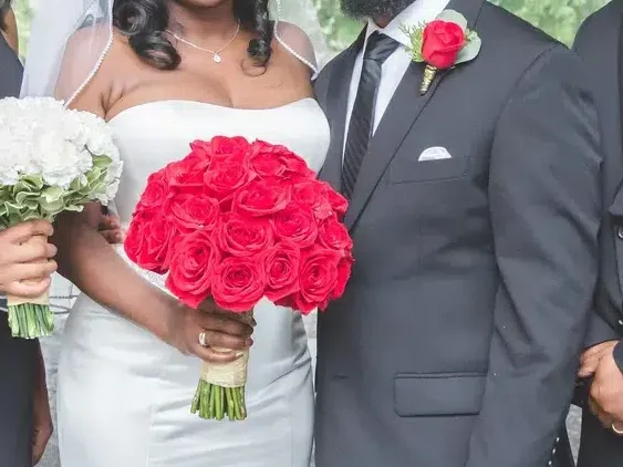 bride and groom with their bridal party, all smiling, with the bride holding a vibrant bouquet of red roses and the bridesmaid with white hydrangeas, courtesy of flowers for weddings.