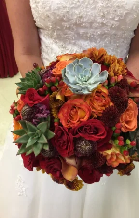 Bride holding a contemporary bridal bouquet featuring succulents, red roses, and orange blooms.
