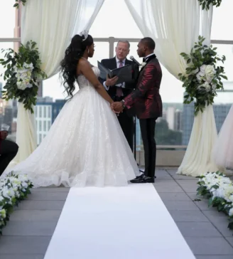 Bride and groom holding hands during their wedding ceremony with an officiant on a rooftop setting.