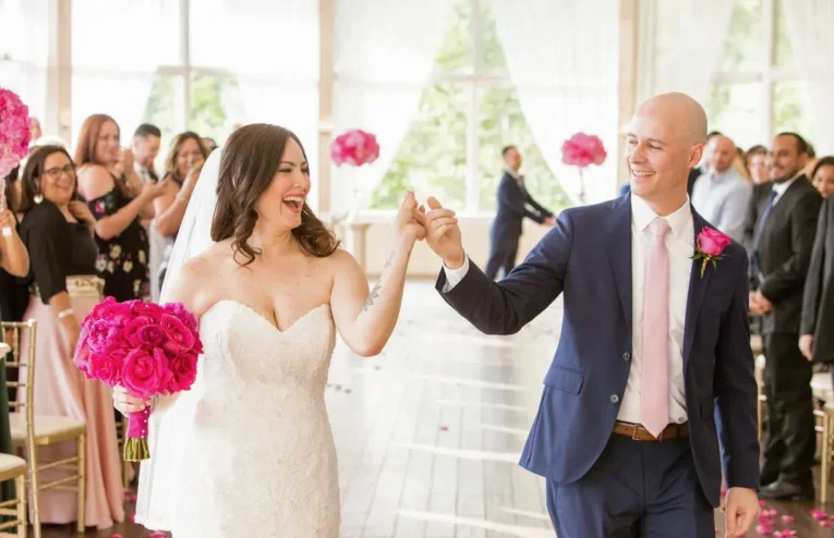 Bride and groom celebrate their marriage, holding hands and smiling, with the bride holding a bouquet of vibrant pink peonies.