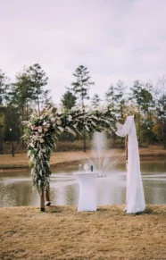 Floral arch and table setup by a lake for a wedding ceremony.