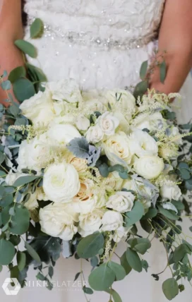 luxurious wedding bouquet featuring a mix of white roses, cream ranunculus, and abundant eucalyptus leaves.