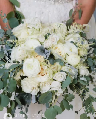 luxurious wedding bouquet featuring a mix of white roses, cream ranunculus, and abundant eucalyptus leaves.