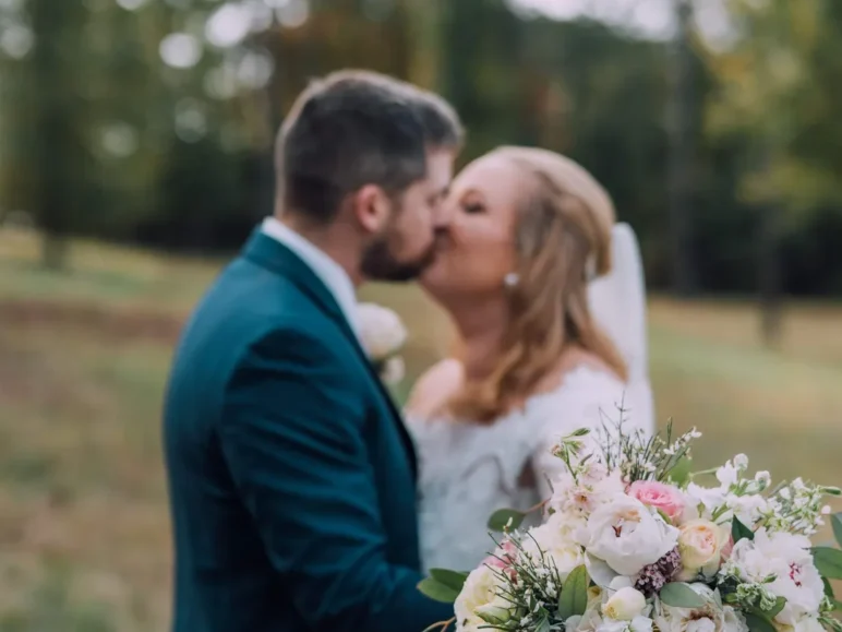 Bride and groom share a kiss while holding a bouquet of flowers