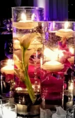 Floating candle centerpiece with flowers in tall glass vases on a dinner table.